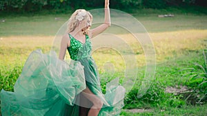 Nice pregnant girl with blond hair with white orchids shows her bare leg in the cut of a long fluttering flying green