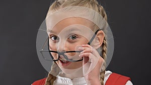 Nice schoolgirl in eyeglasses winking at camera against blackboard, education