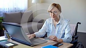 Nice senior woman in wheelchair typing card number on laptop, paying bills