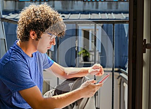 Nice shot of a young Caucasian man intent on consulting his cell phone. He is sitting on the edge of an attic window, the natural