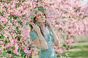 Nice slim young girl in blue dress and straw hat dream in blooming  garden