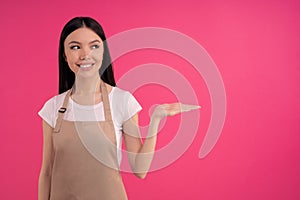 Nice stylish brunette asian girl, barista in casual tshirt and apron, holds a conditional object in her hand. free space for your