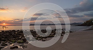 Nice sunset or sunrise moment sunbeam goes through rocky beach scene with hills in distance in Sumbawa, Indonesia