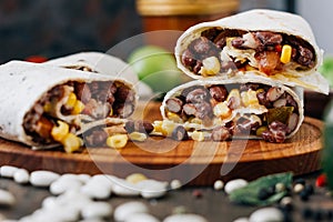 Nice vegetarian burrito over black table on wooden board.