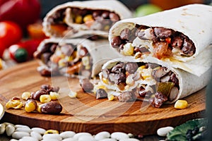 Nice vegetarian burrito over black table on wooden board.