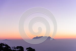 Nice white fog at the mountain in the morning with sunrises light and tree silhouette and small mountain in background