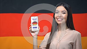 Nice woman holding phone with language study app, German flag on background