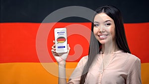 Nice woman holding phone with language study app, German flag on background