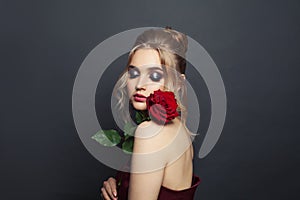 Nice woman model with blonde hair and makeup holding red rose flower on black background