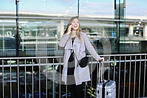 Nice woman standing with valise and talking by smartpone near airport.