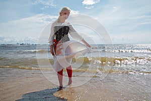 Nice woman in vintage dress holding red sail boat against sea and sky