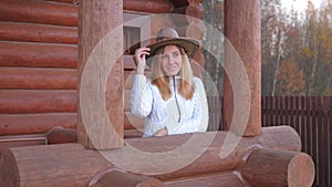 Nice Woman In A White Sweater And A Cowboy Hat On The Veranda Of A Wooden House