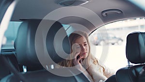 Nice young blonde woman sits talking on her phone in her brand-new car with modern inside and leather seats and the car