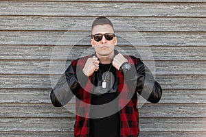Nice young hipster man in a fashionable plaid jacket in a black t-shirt with stylish sunglasses is posing