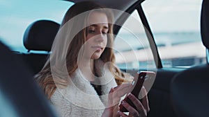 Nice young lady with blue eyes and loose blonde hair using a mobile app to send a message to her friend while driving in