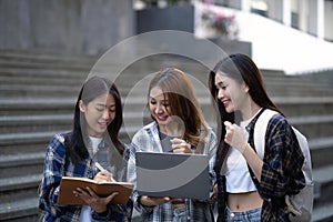 Nice young students use laptop after class sitting outdoors. girls wear casual clothes in spring. Concept of modern