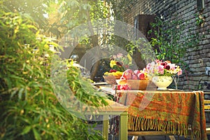 Nicely decorated wooden table full of different kinds of fruits inside shiny beautiful garden with lots of flowers and green