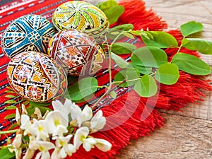 Nicely hand decorated romanian orthodox easter eggs with traditional motifs on a red cloth with acacia flowers aside