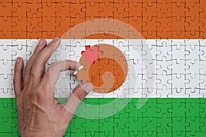 Niger flag is depicted on a puzzle, which the man`s hand completes to fold
