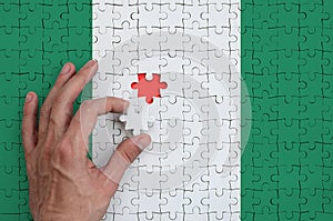 Nigeria flag is depicted on a puzzle, which the man`s hand completes to fold