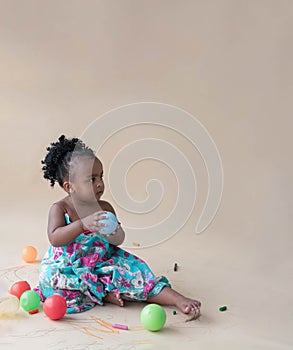 Nigerian baby girl sitting on the floor, holding and looking at a blue crayons