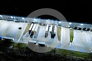 Night Aerial view of goods warehouse. Logistics center in industrial city zone from above. Aerial view of trucks loading at