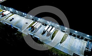 Night Aerial view of goods warehouse. Logistics center in industrial city zone from above. Aerial view of trucks loading at