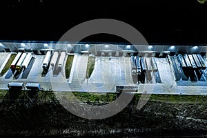 Night Aerial view of goods warehouse. Logistics center in industrial city zone from above. Aerial view of trucks loading at