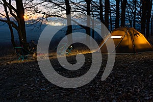 Night camp in the forest. light in the camping tent and portable chairs and aluminum table. Cold autumn. concept of vacation and