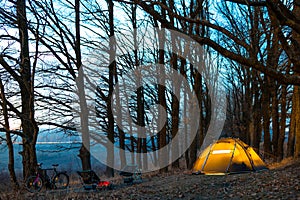 Night camp in the forest. light in the camping tent and portable chairs and aluminum table. Cold autumn. concept of vacation and