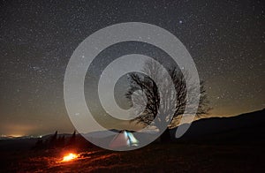 Night camping in the mountains. Hikers having a rest in tourist tent under starry sky near campfire