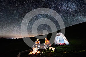 Couple tourists near campfire and tents under night sky full of stars and milky way