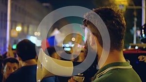 In the night city a man with a loudspeaker looks at the crowd of protesters