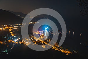 Night city. View of the village from the top of the mountain, streets and lights, a bay with boats. Travel and vacation concept in