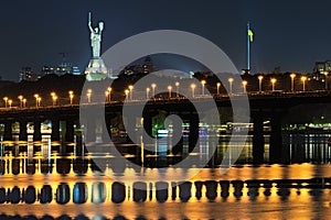 Night cityscape panorama of illuminated Paton bridge over Dnieper river. Famous Motherland monument at the background