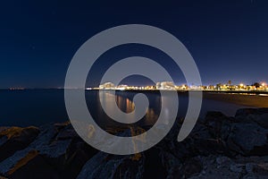 Night cityscape with sea and rocks in foreground and night star sky, night urban landscape of a Spanish city. Travel destination