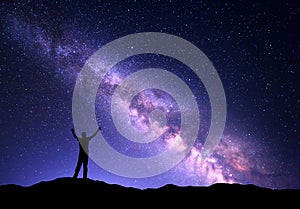 Night colorful landscape with purple Milky Way and silhouette of a standing sporty man with raised up arms on the mountain