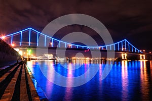 Night european city in colorful lights and reflection in water, Kiev, Ukraine. Pedestrian bridge across the Dnieper river