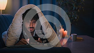 Night at home Hispanic guy gadget internet social media addict tired sleepy man reading news in social media shocked