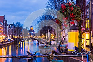 Night illumination of Amsterdam canal and bridge with typical dutch houses, boats and bicycles.