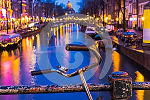 Night illumination of Amsterdam canal and bridge with typical dutch houses, boats and bicycles.