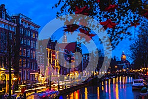 Night illumination of Amsterdam canal and bridge with typical dutch houses, boats and bicycles.