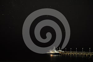 Small pleasure boat moored to a pier near the sea coast. Starry night sky over the sea