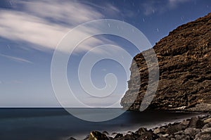 Night landscape with star trails. Beach with rocks and moving waves. Long exposure. Cliffs in the sea near Tasartico. Gran Canaria