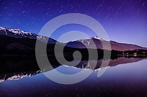 Night landscape with star trails and snow capped mountain with perfect reflection in a lake and amazing blue and purple colours