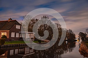 Night landscape with starry sky in the Dutch village of Streefkerk. Houses with bright light reflecting in the shine of the water