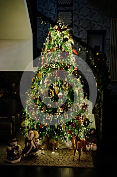 Night. a large elegant Christmas tree with a garland in the house by the stairs.