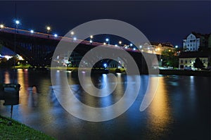 Night light landscape of Old Bridge (also named the State) over Drava River. Lantern\'s lights reflected in water