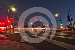 Night lights of a commuter train streak across a street intersection next to a crosswalk.