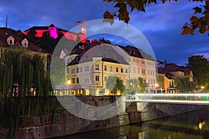 Night lights landscape of old city. Illuminated medieval buildings near Ljubljanica River and ancient Ljubljana Castle at the top
